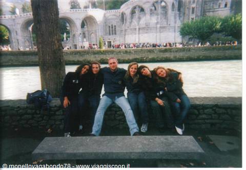 Friends posing on a stone wall in front of Lourdes sanctuary