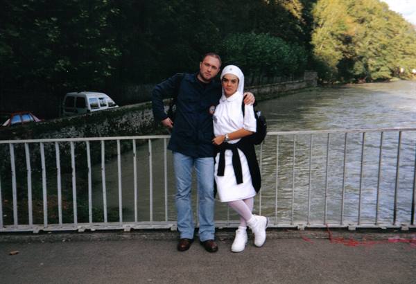 Couple posing on an iron railing bridge by a tree-lined river