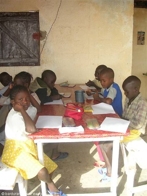 Children draw at a red-clothed table against a yellow wall