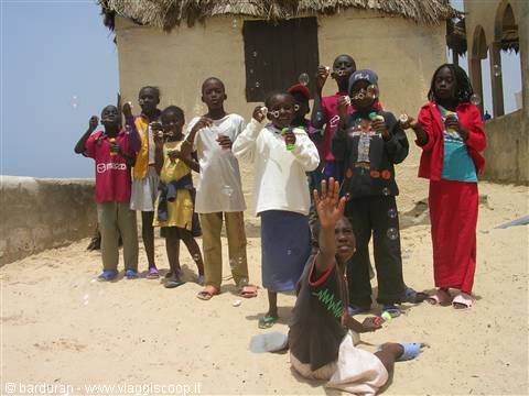 African children posing on the sand in front of thatched-roof houses