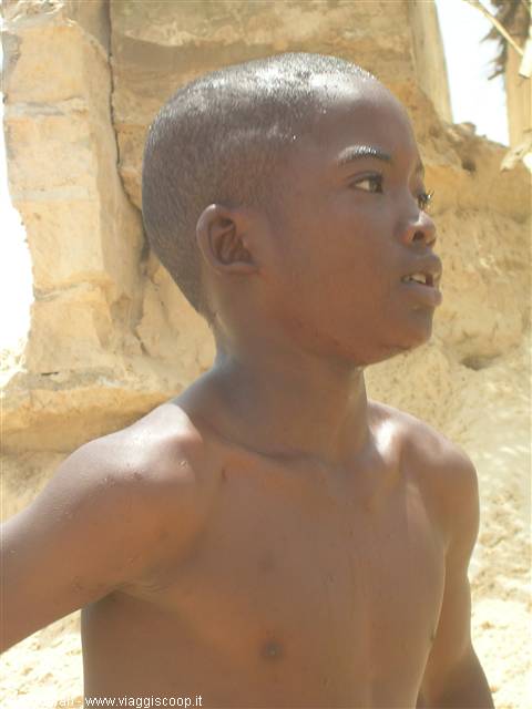 Shirtless boy standing in front of sunlit sandy rock wall