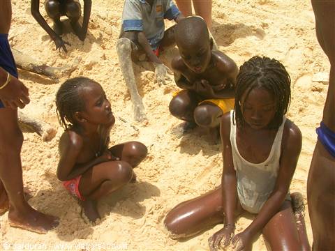 Children crouching on beach sand under bright sunlight