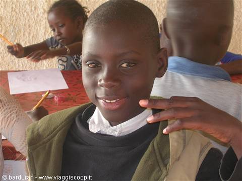 Smiling boy in green vest drawing with classmates in classroom