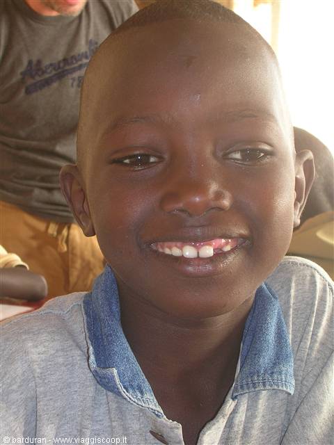Smiling boy with protruding teeth, blue shirt, natural light indoors