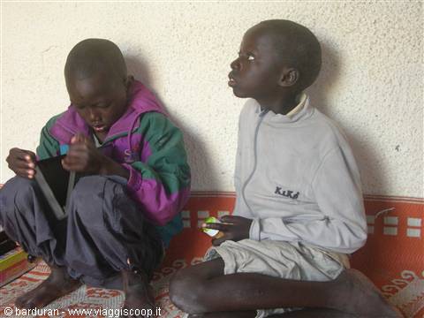 Two boys sitting on orange carpet against white wall, one looking up