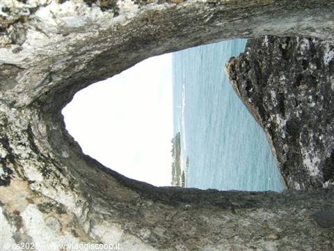 Turquoise sea seen through an opening in dark rough rock
