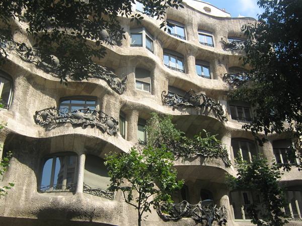 Wavy stone facade of Casa Milà, wrought-iron balconies framed by green trees