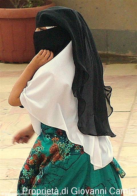 Woman in black niqab and green floral dress walking outdoors