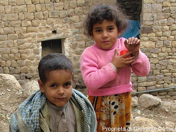 Girl in pink sweater and boy with keffiyeh in front of stone wall