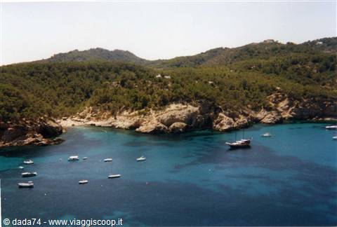 Boats anchored in turquoise cove surrounded by rocks and green hills