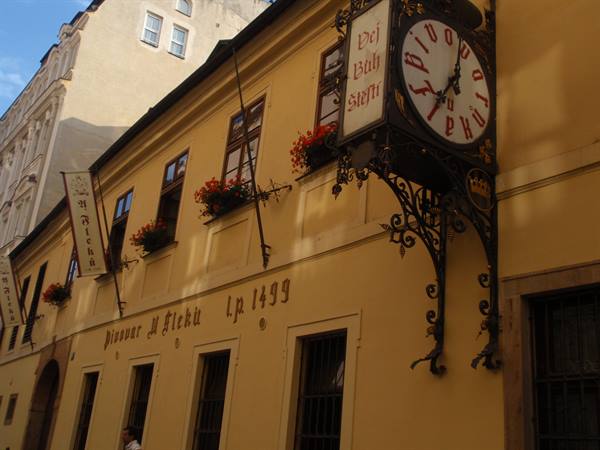 Wrought-iron sign with clock on the yellow facade of U Fleků brewery, Prague