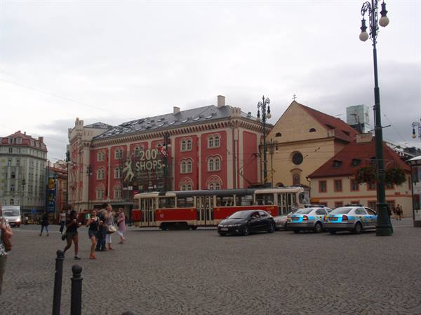 Red tram and taxis in Prague's Republic Square, historic buildings under grey sky