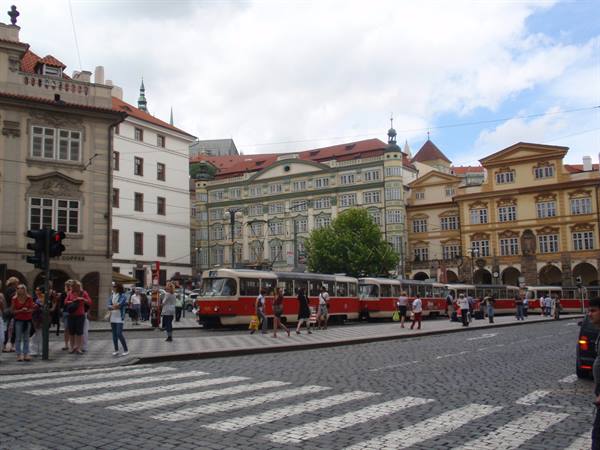 Red trams and pedestrians crossing a square with historic houses in Prague