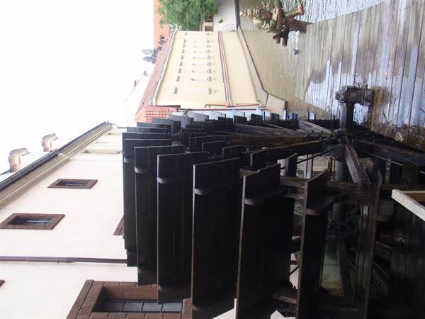 Large dark wooden waterwheel next to a building, canal water flowing