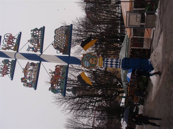 Blue and white Bavarian maypole with carved figures at a snowy market