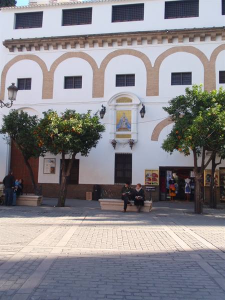 Cobblestone square with orange trees before a white arched facade and Virgin niche