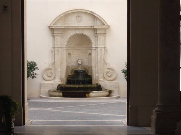 Stone fountain with sculpted face seen through a dark archway