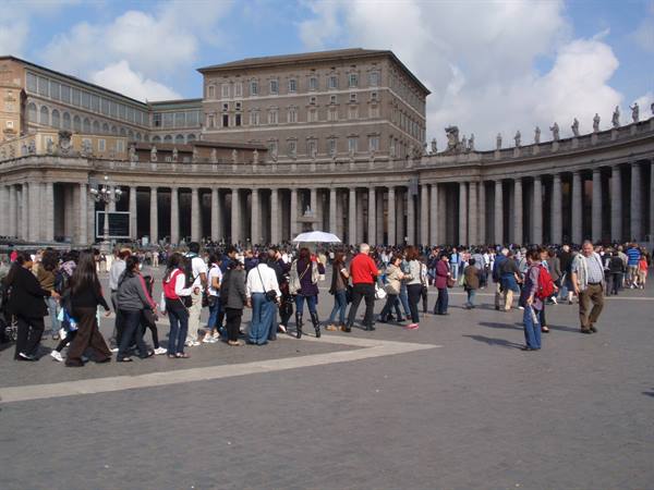 Tourists walk in front of Bernini's colonnade at St. Peter's Square