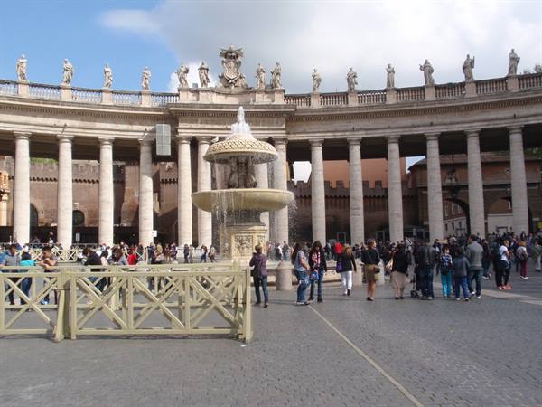 Bernini fountain and colonnade in St. Peter's Square, tourists strolling under cloudy sky