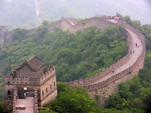Tourists walk along the Great Wall of China among stone towers and mist