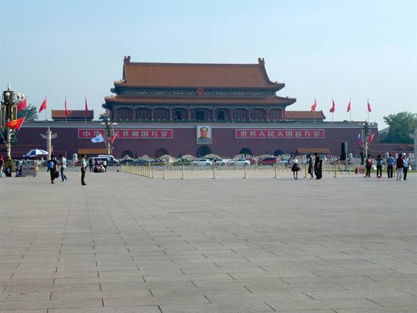 Tourists walk across Tiananmen Square before the gate with Mao's portrait