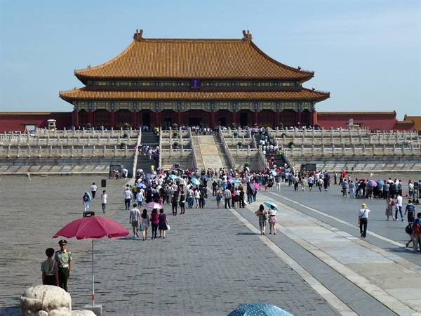 Tourists with umbrellas cross the square before the golden-roofed Forbidden City palace