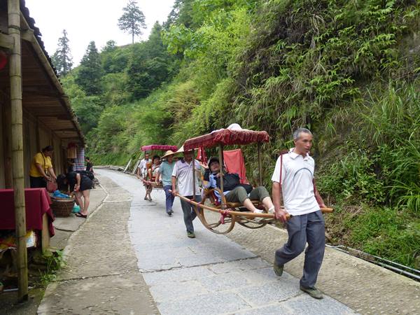 Bearers carry tourists in red-covered bamboo sedan chairs on stone village path
