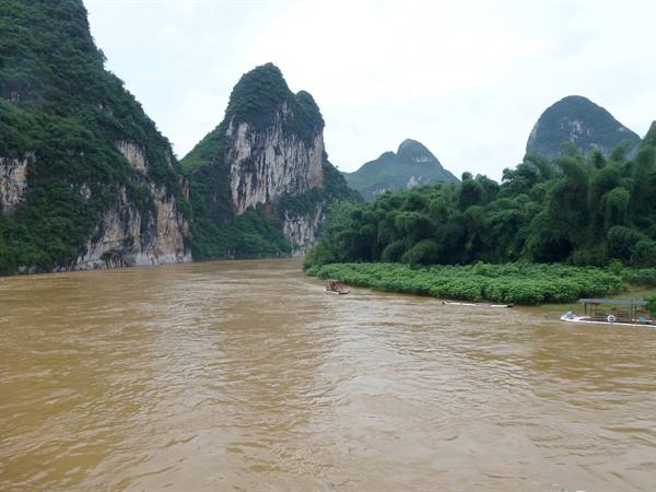 Muddy Li River winding between green karst peaks, wooden boats on the bank