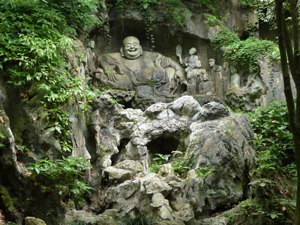 Carved laughing Buddha in rock cliff at Feilai Feng, Lingyin Temple, soft forest light