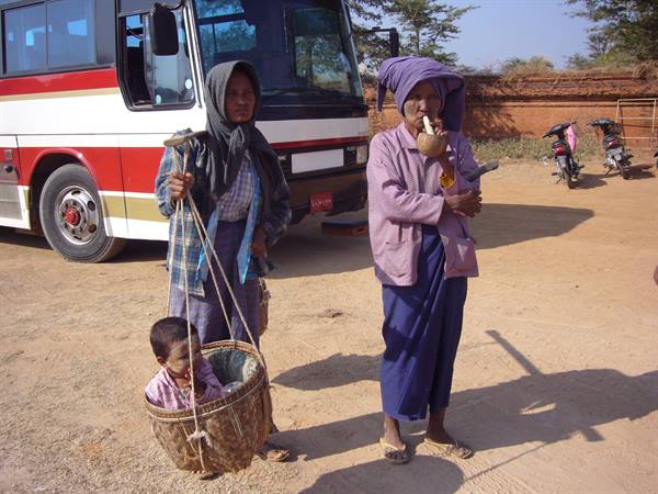 Burmese women beside a tour bus, one carries a child in woven basket
