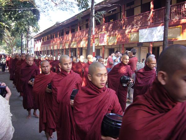 Buddhist monks in maroon robes queue with alms bowls at Mahagandayon monastery