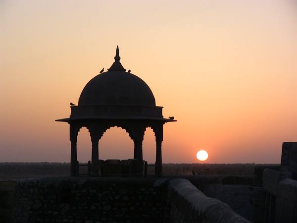 Stone pavilion with domed roof silhouetted at dusk, birds perched, low sun on horizon