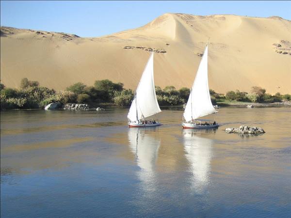 Two white-sailed feluccas on the Nile in front of sand dunes