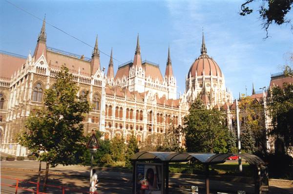 Budapest Parliament among trees, neo-Gothic dome and spires under blue sky