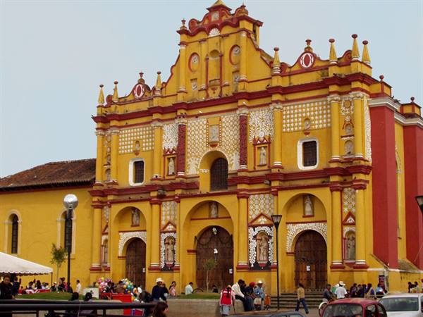 Yellow and red baroque church with decorated facade, people sitting on the square