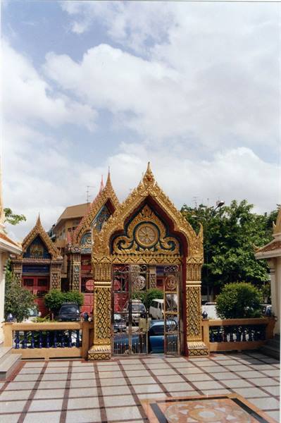 Golden Buddhist temple gate with ornate spires, marble courtyard beneath cloudy sky