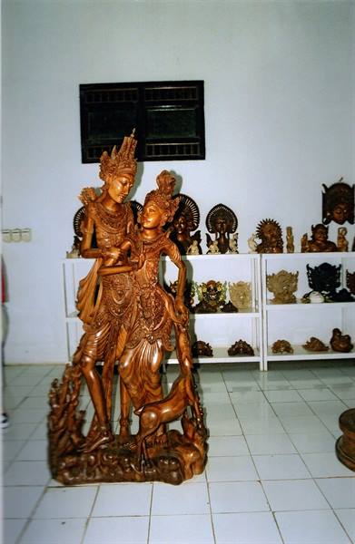 Carved wooden dancing couple statue, masks displayed on white shelves