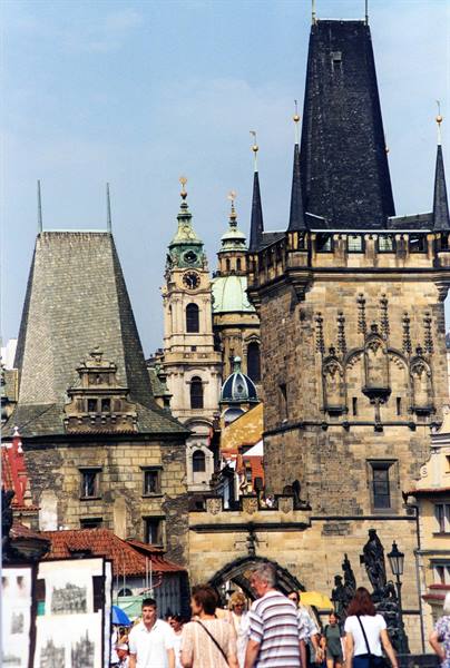 Tourists walk beneath the gothic stone tower of Charles Bridge, Prague
