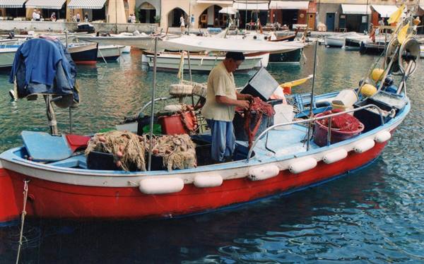 Fisherman mends nets on a red boat in Camogli harbor