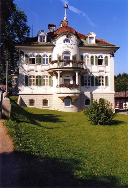 White villa with flowering balconies, green shutters and lawn under blue sky
