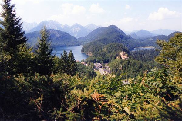 Hohenschwangau Castle among trees with Alpsee lake and Bavarian mountains