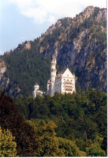 Neuschwanstein castle with towers rising above green forest and rocky mountain