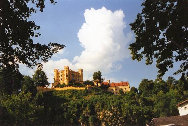 Yellow Hohenschwangau Castle on a wooded hill framed by trees