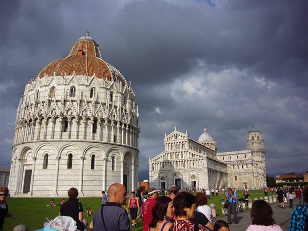 Tourists on green Piazza dei Miracoli in Pisa, baptistery and cathedral under dark clouds
