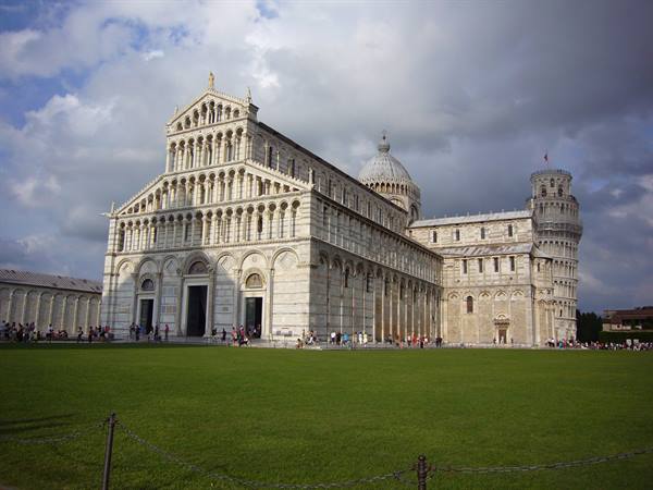 Pisa Cathedral in white marble with the Leaning Tower, tourists on lawn under clouds