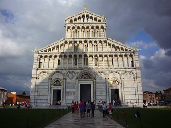 Tourists before the marble facade of Pisa Cathedral under cloudy sky