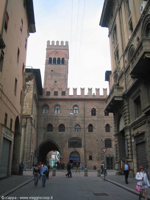 Crenellated brick tower and medieval palace, pedestrians crossing the street in Bologna