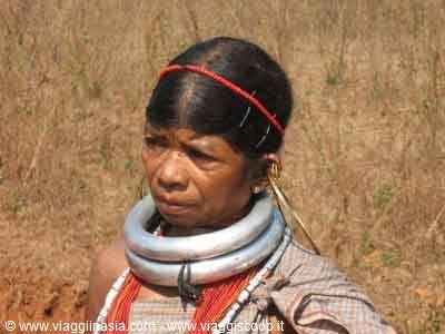 Tribal woman wearing silver neck rings and gold earrings, dry fields behind