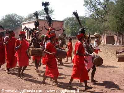 Men in red robes and tribal headdresses drum during a village ceremony