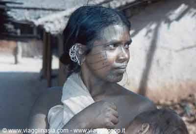 Tribal woman with silver earrings and facial tattoos in front of village houses